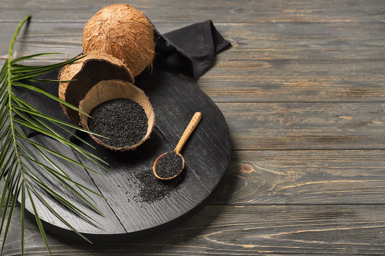 Coconut Shells and Spoon with Activated Carbon on Wooden Background